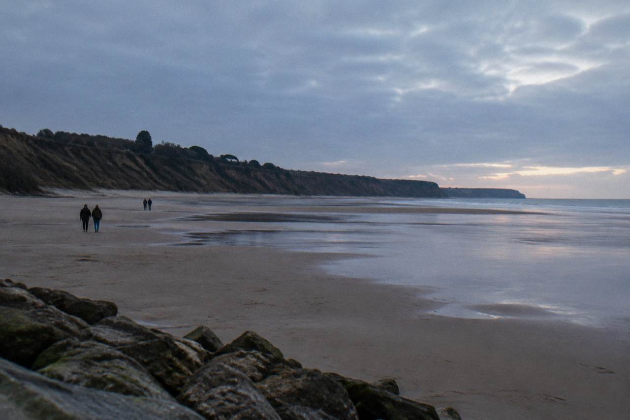 Wide view of Omaha Beach at low tide with sand flats stretching to the bluff line