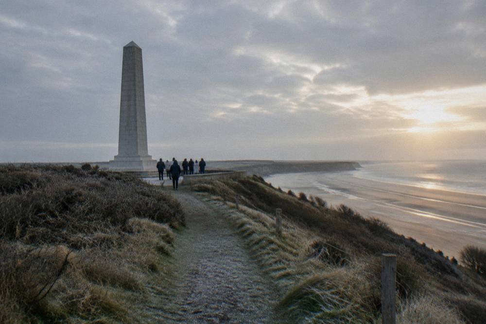 Light stone memorial monument on the bluff above a wide Normandy beach