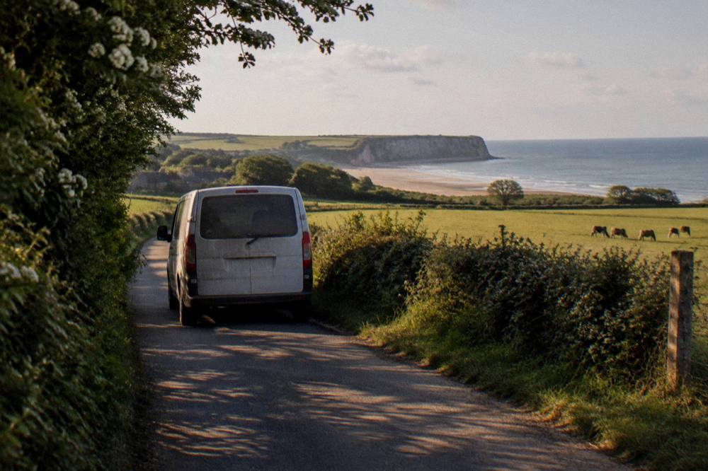 Minivan parked on a small lane beside green Normandy fields
