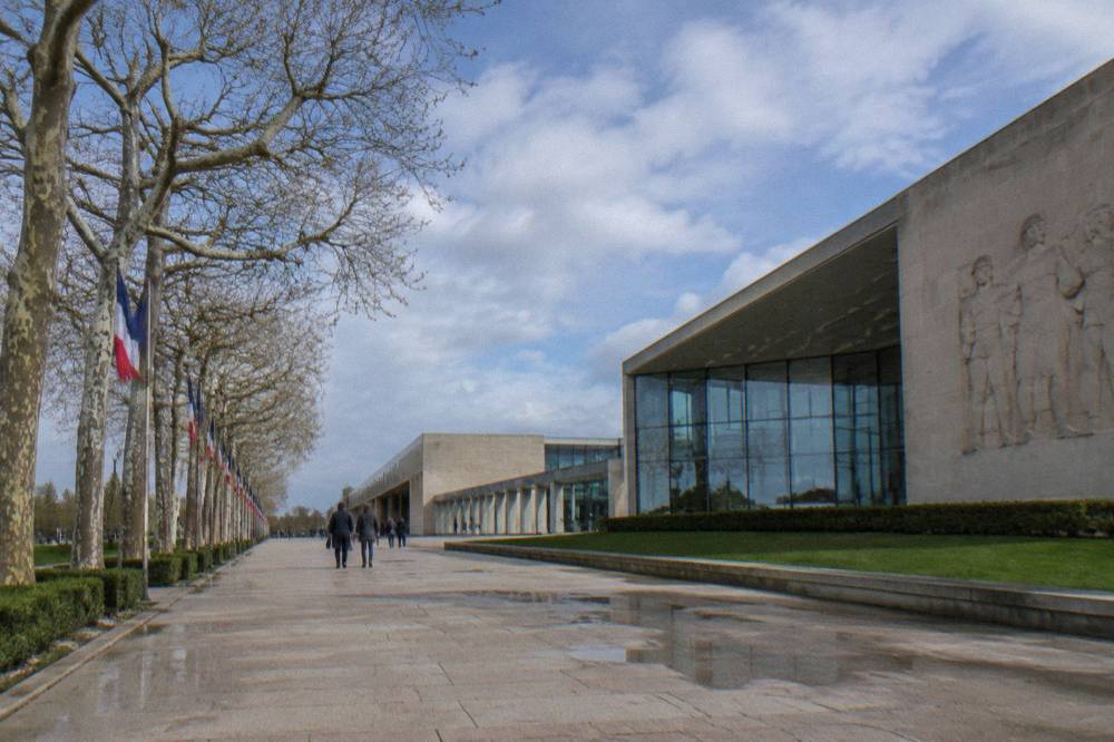 A modern museum esplanade with pale stone buildings under a wide sky in Caen