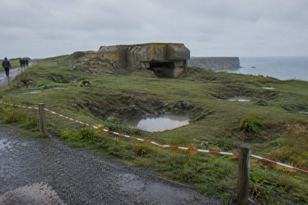 Windswept clifftop field at Pointe du Hoc with cratered ground and a concrete bunker