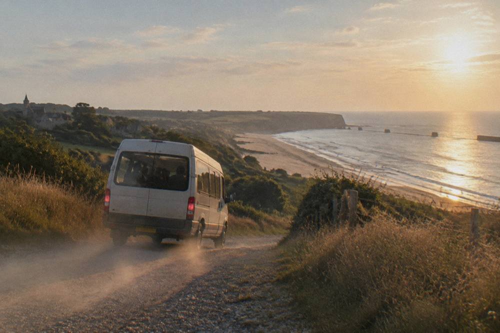A small minibus parked beside a hedgerow-lined lane near the Normandy landing beaches