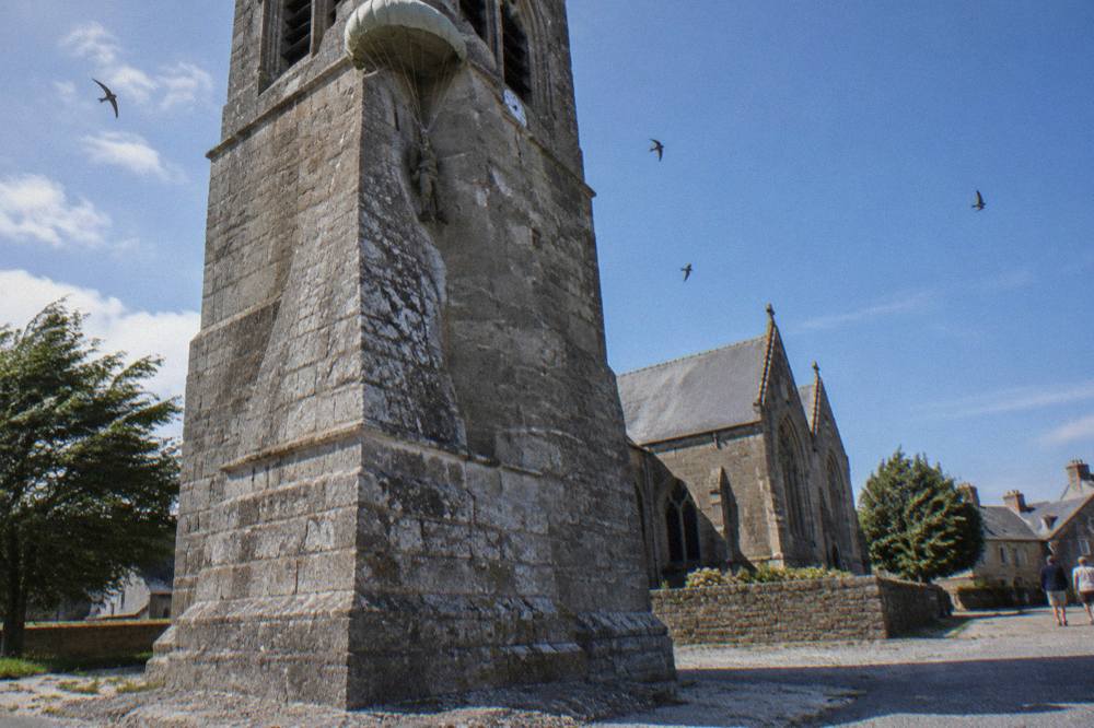 Parachute and harness effigy hanging from the corner of a stone church tower