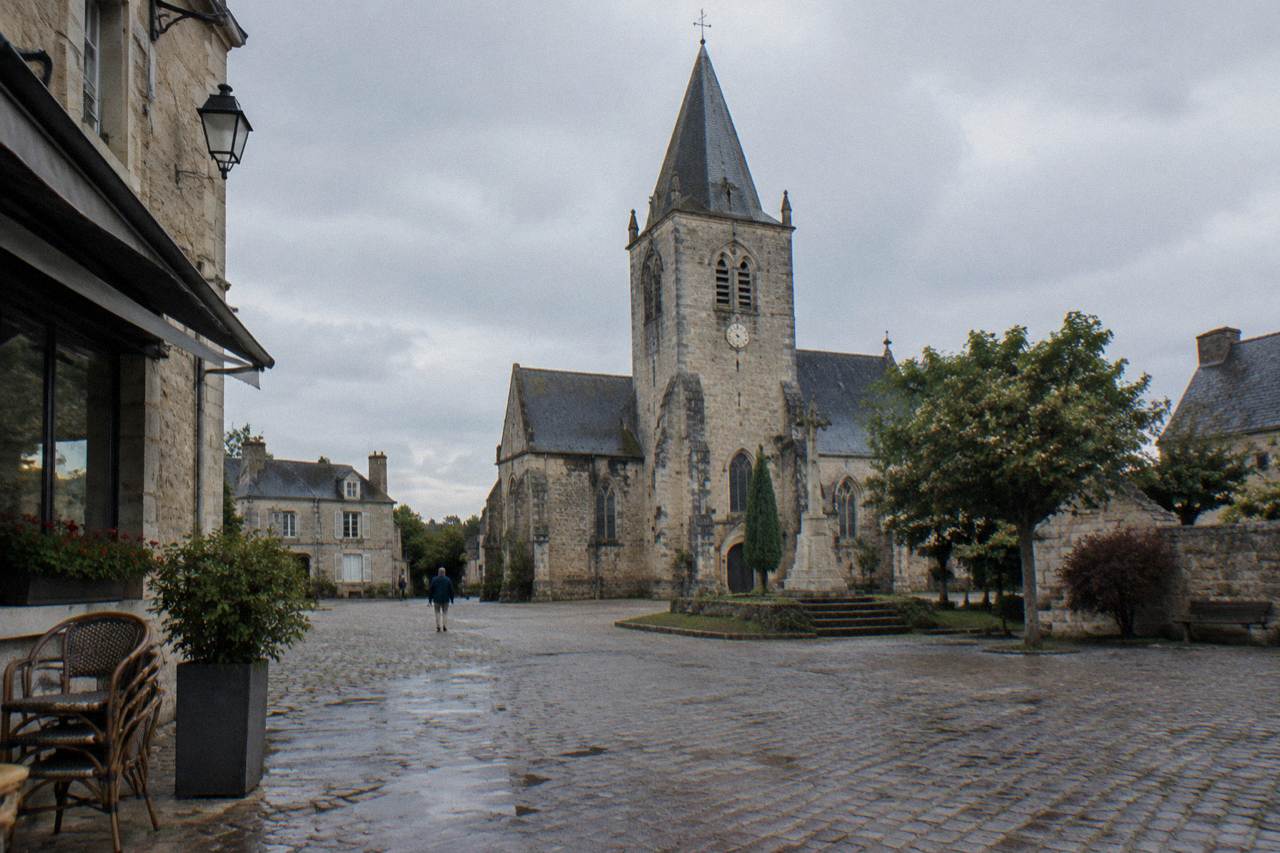 Stone church tower in a small Normandy market square under a gray sky