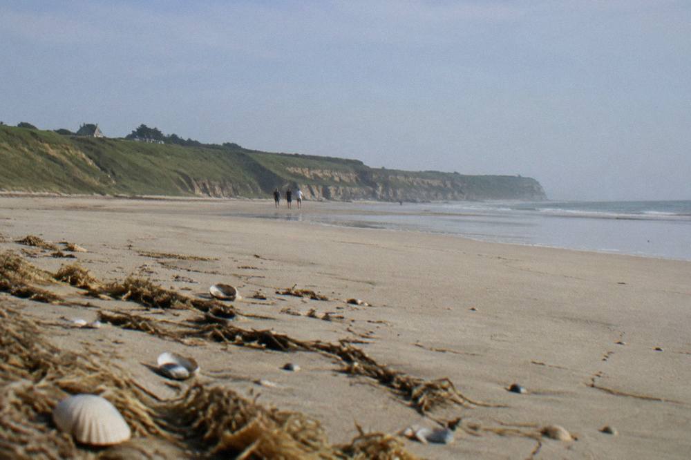 Wide empty sandy beach at low tide beneath grassy bluffs under a gray sky