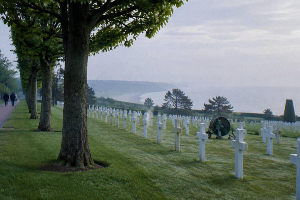 Rows of white marble headstones on a manicured lawn overlooking the sea