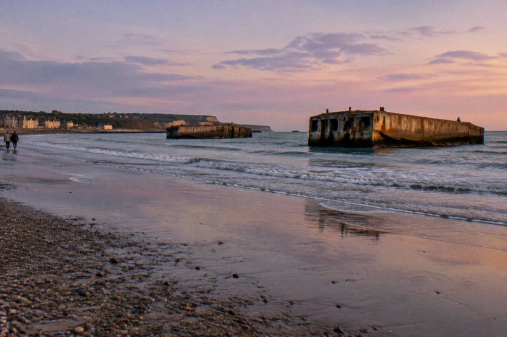 Concrete harbor remains in the shallows at Arromanches under an evening sky