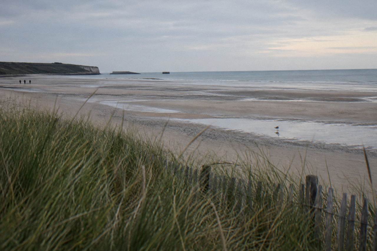 Wide sandy stretch of Utah Beach at low tide with dune grass and a calm gray sea