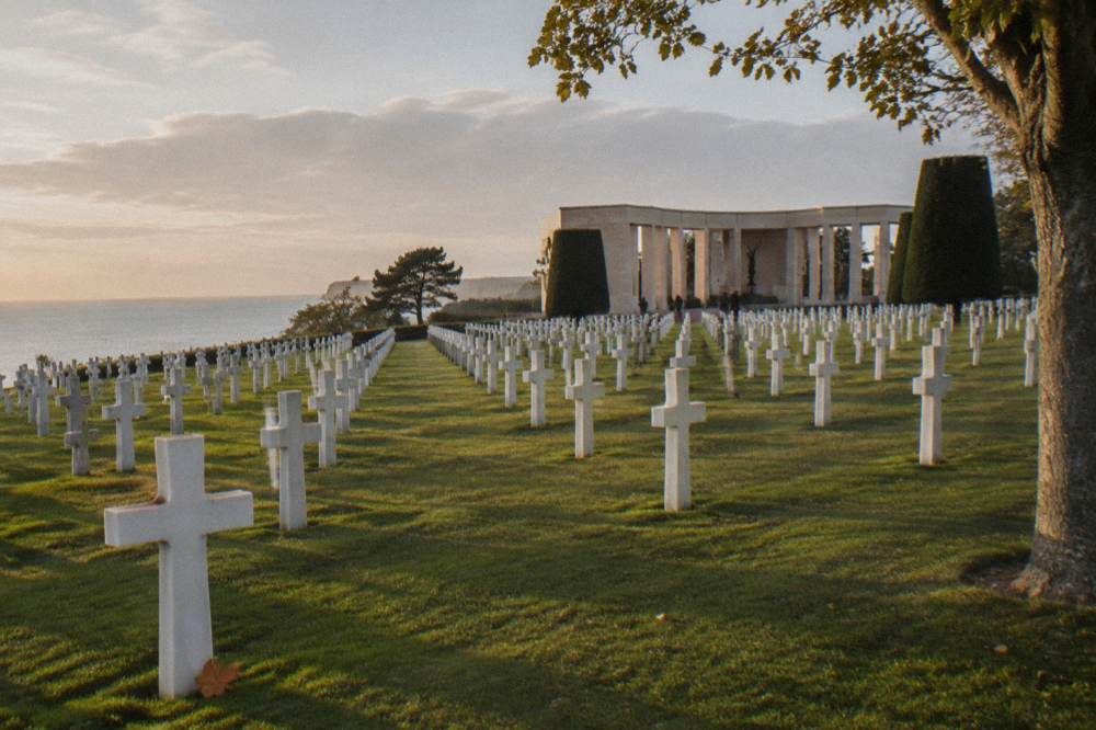 Rows of white marble headstones on a manicured lawn above the sea